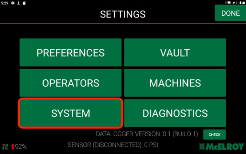 A tablet screen displays a settings menu with six green buttons: Preferences, Vault, Operators, Machines, System (highlighted in red), and Diagnostics. Battery is at 92%, and the Done button is in the top right corner.