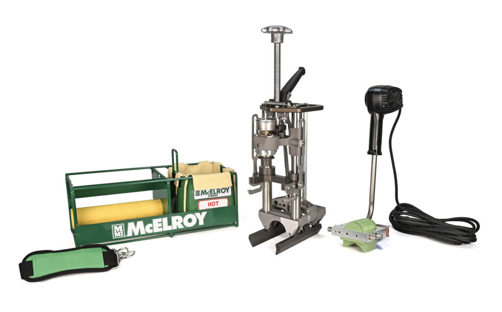 A McElroy pipe fusion tool kit, including a green carrying case, a metal fusion press, a heating tool with a black handle and long cord, and an accessory strap, all arranged on a white background.