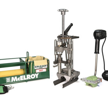 A McElroy pipe fusion tool kit, including a green carrying case, a metal fusion press, a heating tool with a black handle and long cord, and an accessory strap, all arranged on a white background.