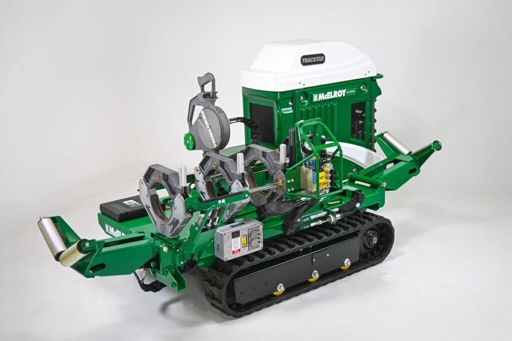 A green and white tracked industrial machine with various controls, metal arms, and attachments, designed for outdoor or construction purposes, against a plain white background.
